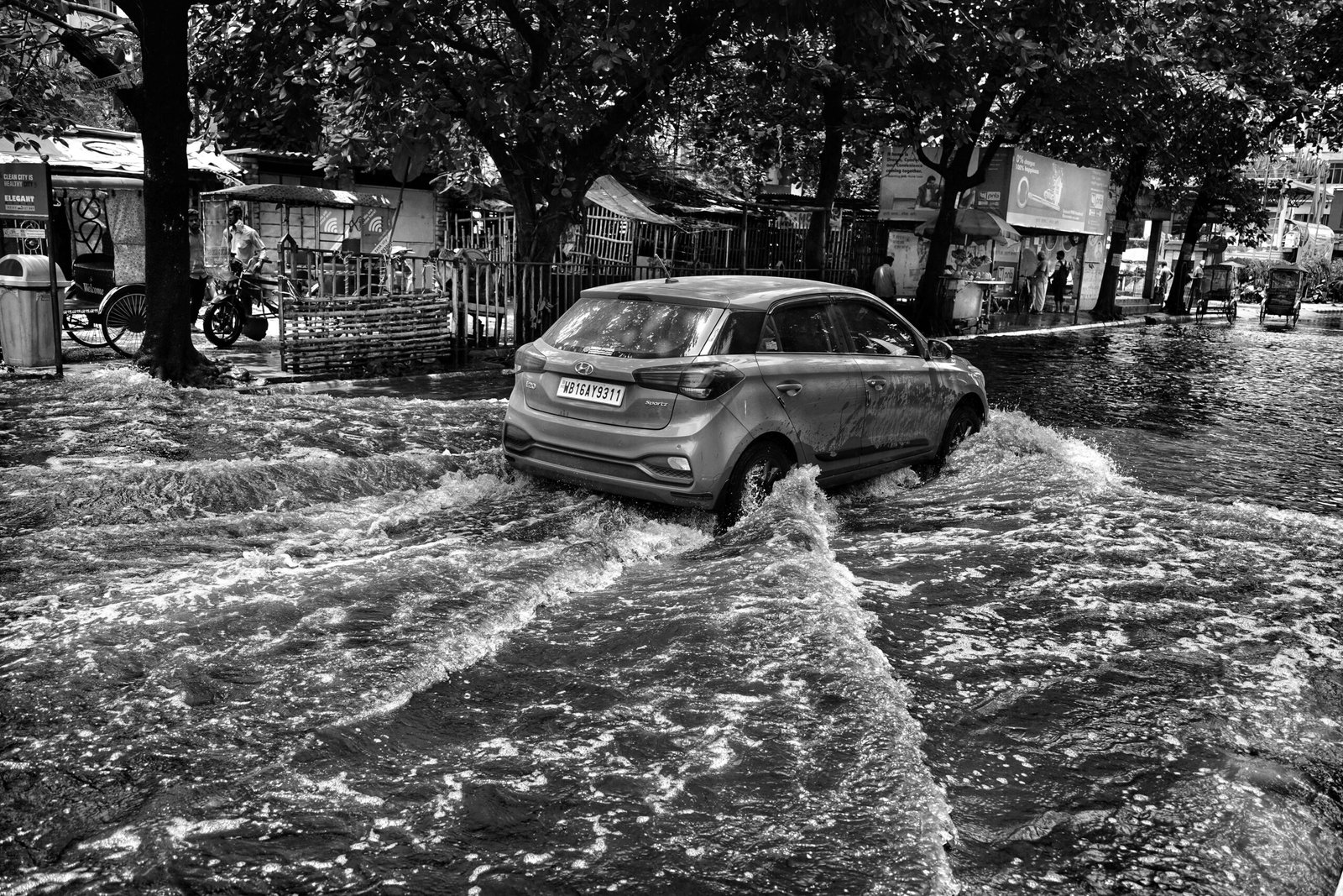 Black and white photo of a car driving through a flooded street in Kolkata, India.